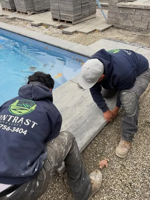 Two crew members setting stone coping along a pool edge