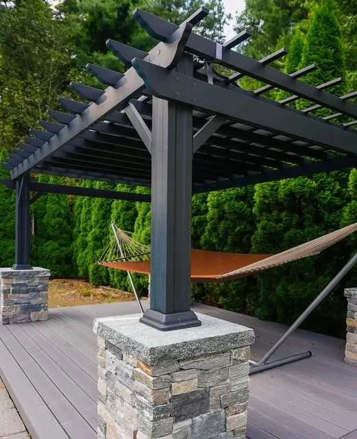 Black pergola with stone-clad posts and a hammock over a composite deck