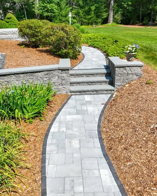 Curved paver walkway with stone steps through mulched planting beds